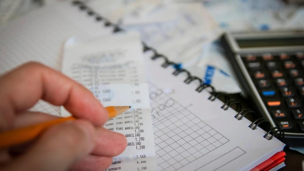 A desk with printed store receipts, a calculator and an open notebook with handwritten figures