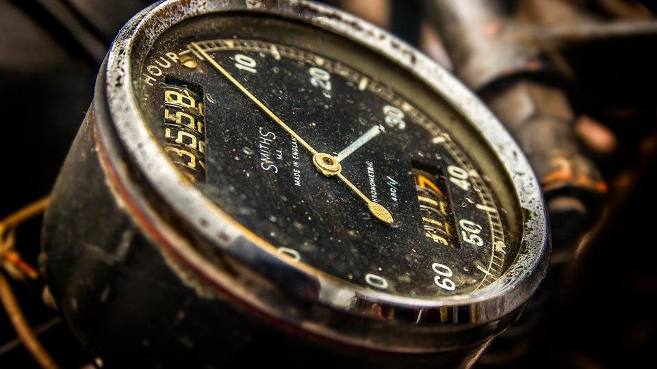 A vintage stopwatch lying on printed web performance charts next to a laptop keyboard under warm lamp light